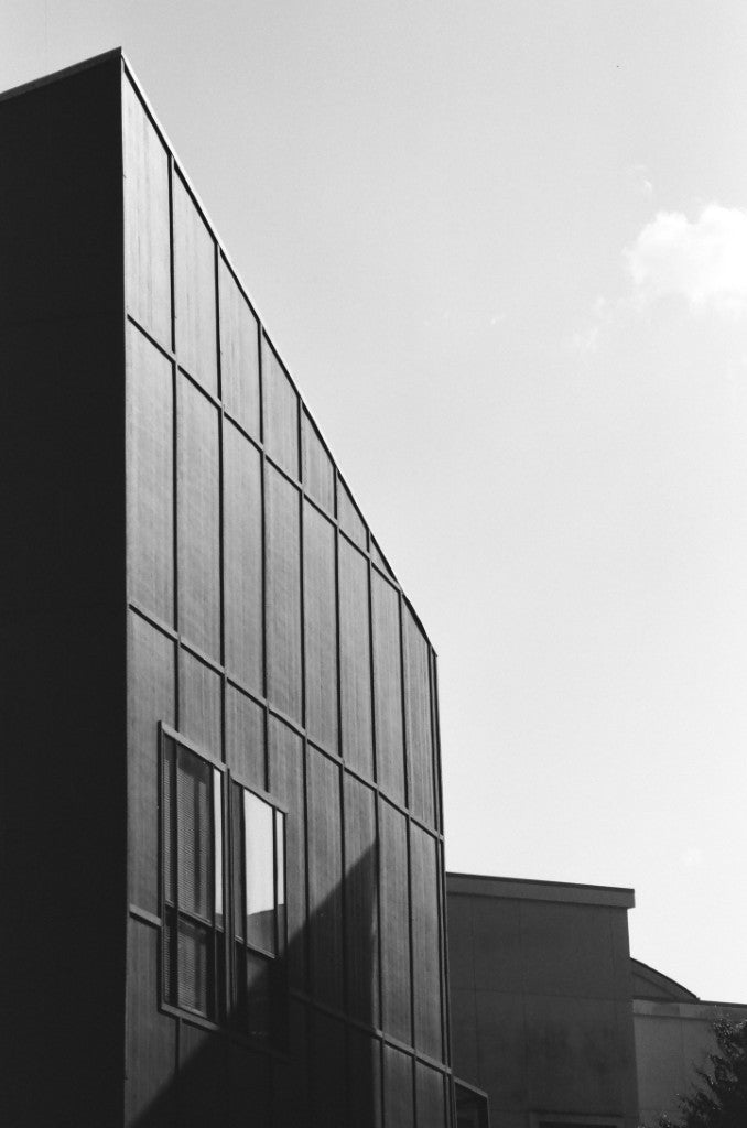 Esquina de un edificio moderno con vista a una fachada de cuadrícula geométrica, fotografiada con película Reflx Lab Zarya 100 (Svema NK-2S) 35mm, revelada en D-76.