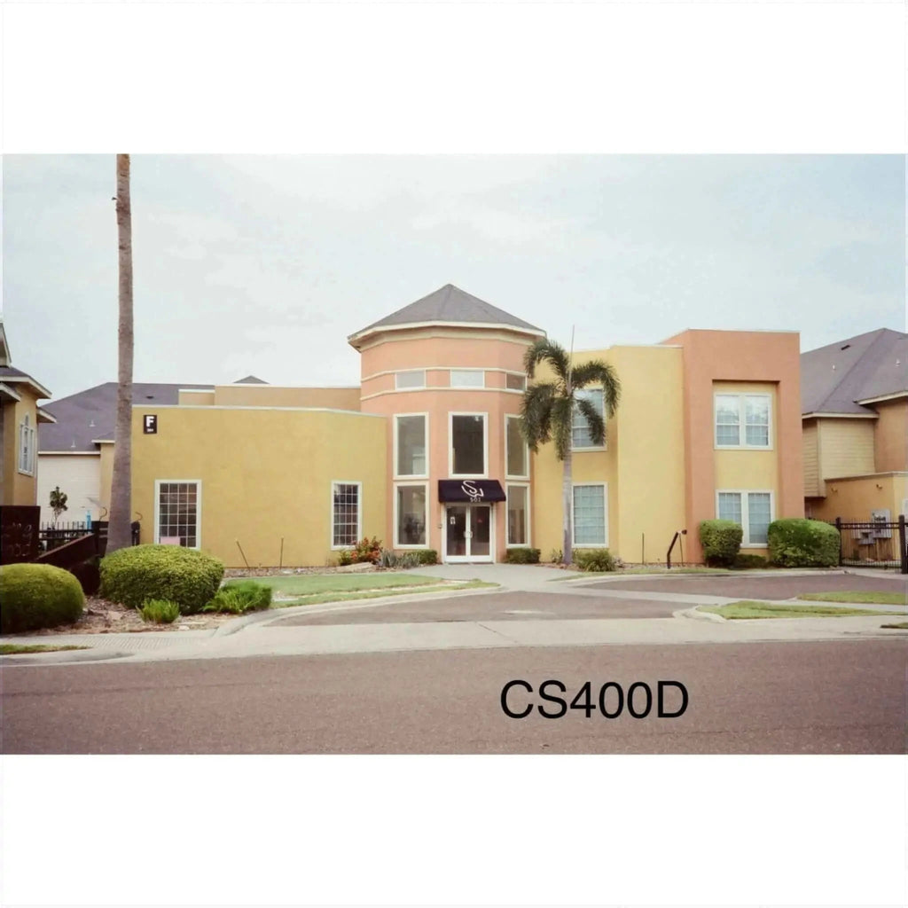 The image shows a two-story building with peach and yellow stucco walls, large windows, and a dark awning over the entrance.