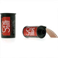Red and black cinestill 35mm film canister with a partially unspooled strip of brown photographic film.