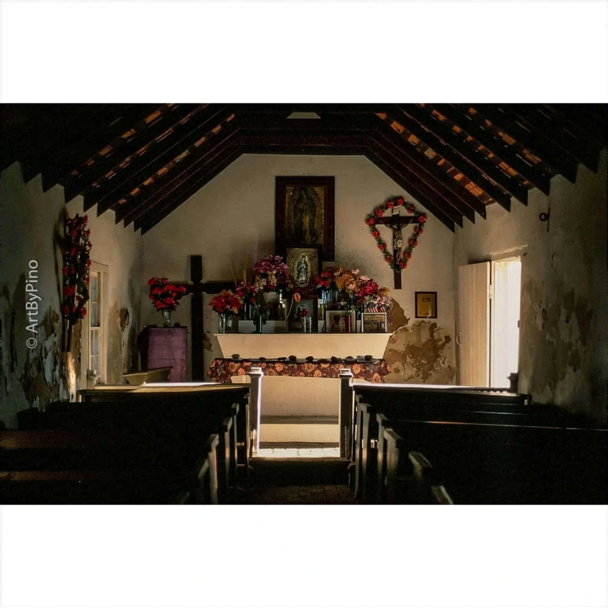 A wooden altar adorned with vibrant red and pink flowers, framed by a dark cross and surrounded by religious icons.