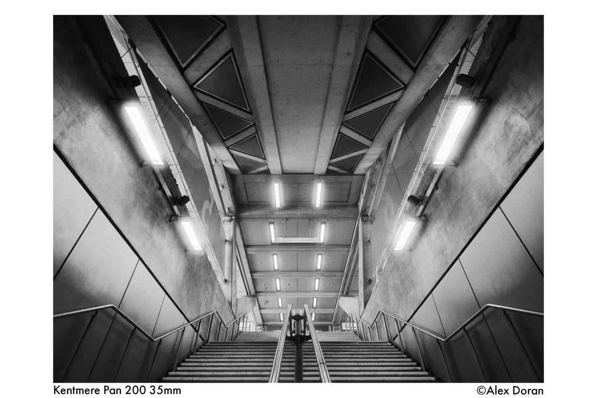 Concrete staircase with metal railings and overhead fluorescent lighting.