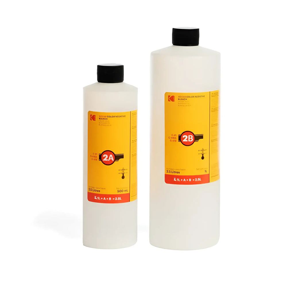 Two translucent plastic bottles of kodak color negative developer, one 500 ml and the other 2.5 litres, both with black caps and bright yellow labels featuring red accents and film strip graphics.