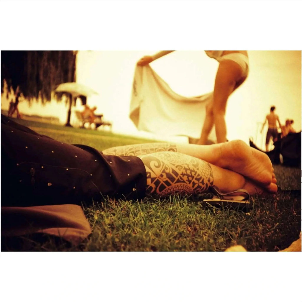 A person’s tattooed forearm and hand resting on grass, featuring intricate black tribal-style patterns.
