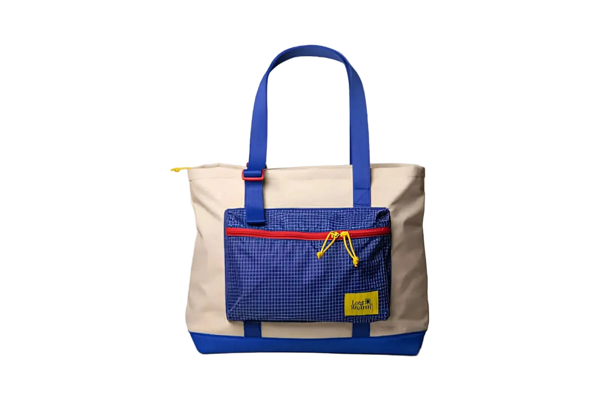 Beige and blue canvas tote bag with a grid-patterned front pocket, red zipper trim, yellow drawstrings, and matching blue handles.