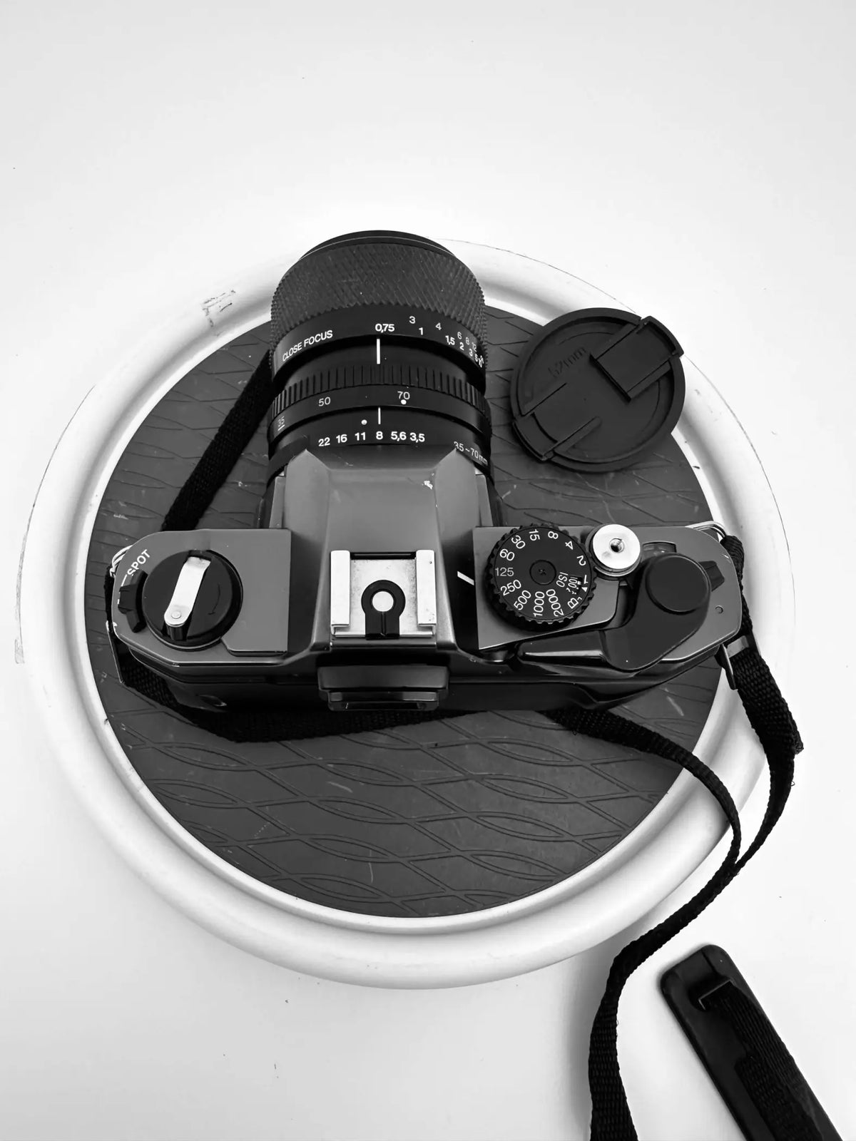 Black dslr camera with a lens cap and strap, resting on a textured circular mat.
