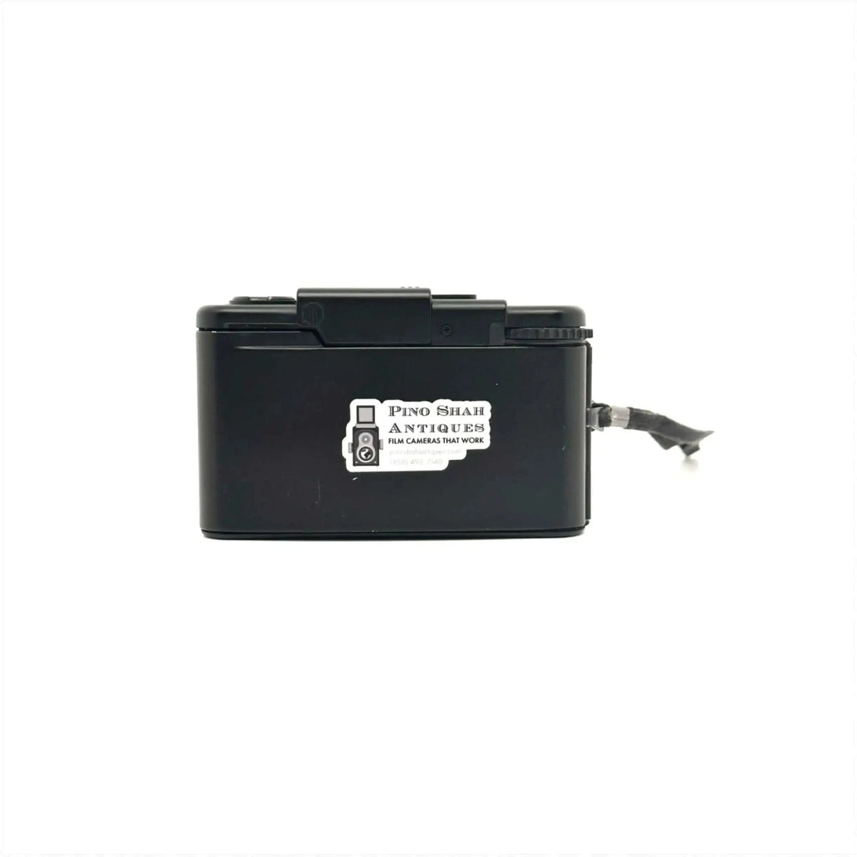 Black plastic box camera with a white sticker reading ’pino shar antiques film cameras that work’ on its side.