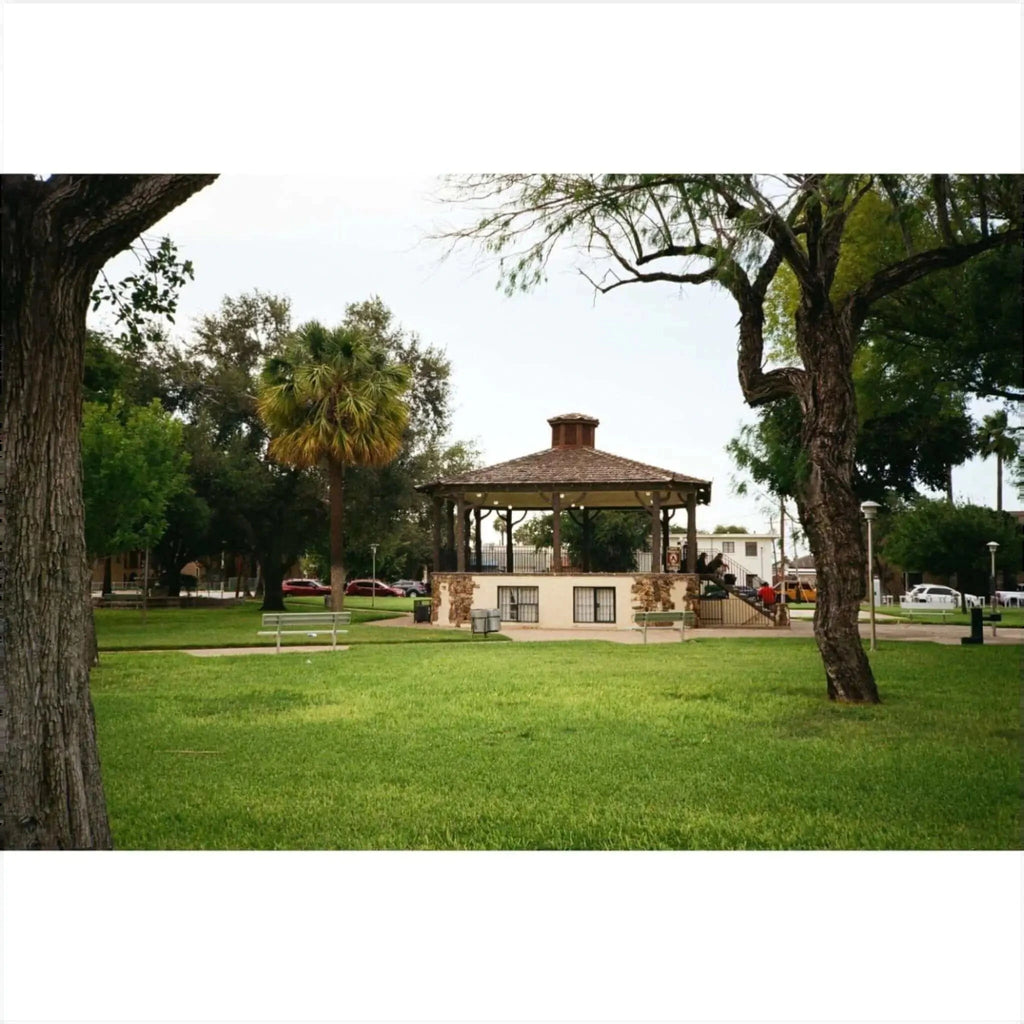 Wooden gazebo with a thatched roof and stone base, surrounded by green grass and trees.