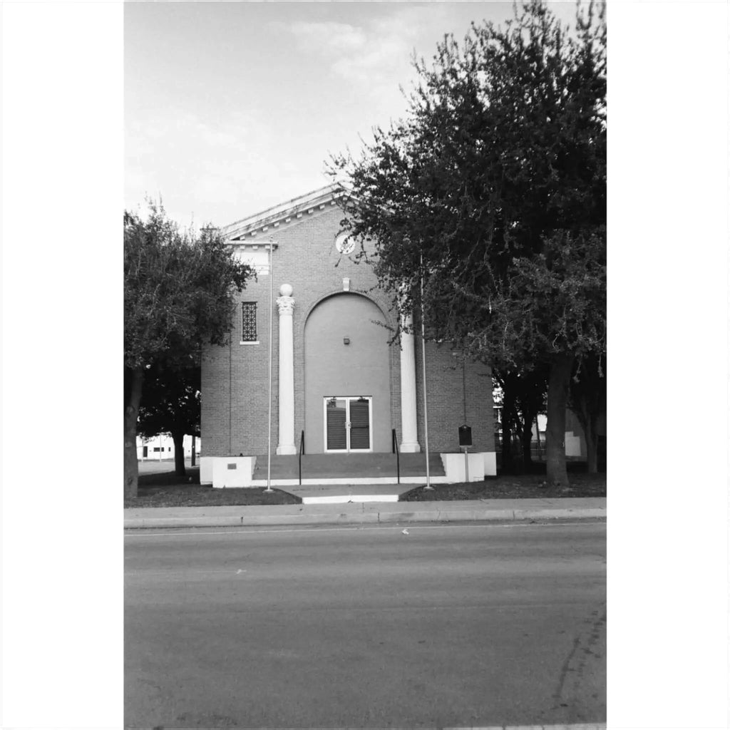 Black and white photograph of a building with trees, featuring a symmetrical arch and detailed architecture.