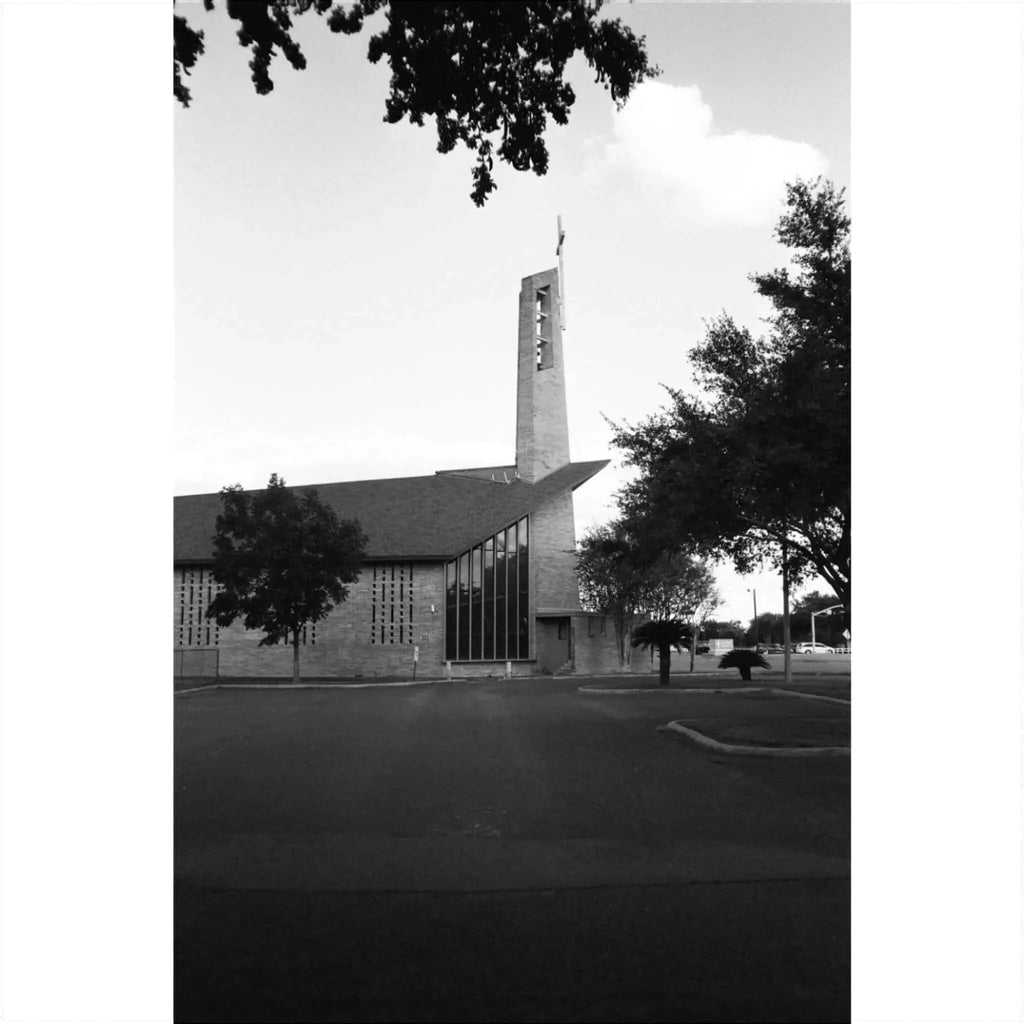Black and white photograph of a modern church building with a tall tower and surrounding trees.