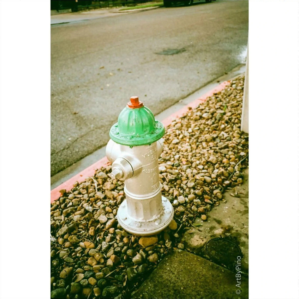 A green and silver fire hydrant on a pebbled sidewalk by the street, showcasing urban infrastructure.
